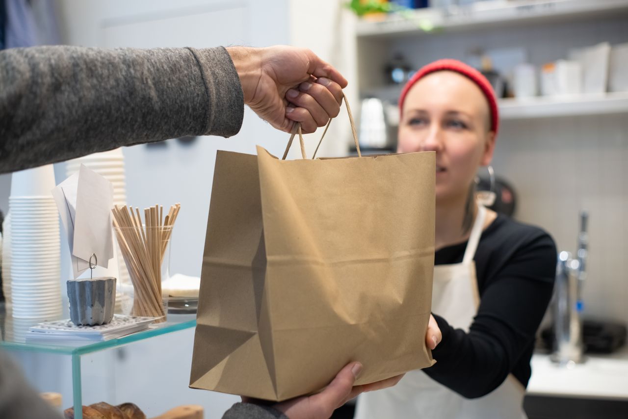Woman handing a takeaway bag to a customer in a Portuguese café. Close-up interaction.